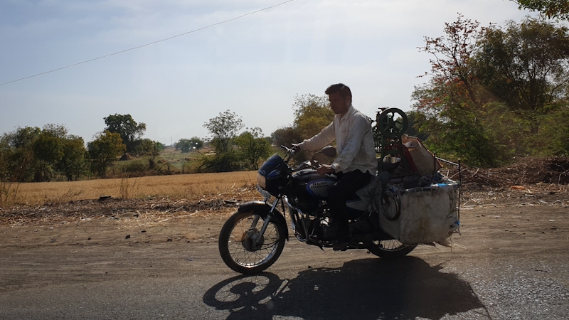 A guy carrying his sugar cane press with him on the bike